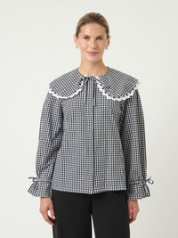 Svart og hvit sjakkmønstret bluse med en stor dekorativ krage, samla ermekanter og knyting ved halsen. Glatt tekstur.