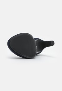 Zapato de tacón de ante azul marino con punta amplia y redondeada y suela de goma negra lisa, que presenta un diseño elegante y un estilo minimalista.