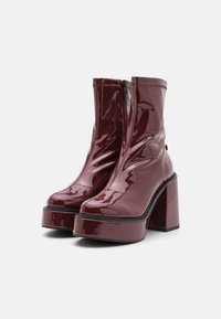 Botas de tobillo de charol burdeos con cremallera frontal, suela de plataforma gruesa y tacón alto tipo bloque. Textura suave y diseño de punta redondeada.