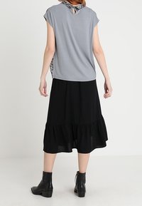 Top gris de manga corta con cuello de estampado de leopardo, combinado con una falda negra larga hasta los tobillos con dobladillo con volantes y botines negros.