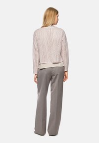 Helles rosa, kurz geschnittenes Sweatshirt mit einem strukturierten Muster, kombiniert mit grauen Nadelstreifen-Hose im weit geschnittenen Stil. Das Sweatshirt hat einen runden Ausschnitt und eine legere Passform.