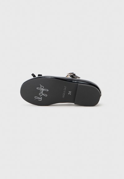 Chaussure en cuir verni noir avec un bout rond, une semelle plate et une boucle décorative. Présente une texture lisse et un logo en relief sur le dessous.