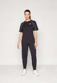 Fekete sportos öltözet, rövid ujjú, fehér részletekkel díszített pólóval és hozzá illő, szűkített szárú nadrággal, légáteresztő anyagból készült.