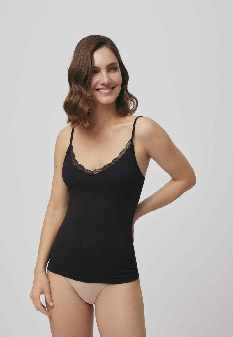 Camiseta negra sin mangas con borde de encaje. Presenta tirantes delgados ajustables y un diseño ceñido. Textura suave, combinada con ropa interior nude debajo.