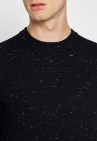 Schwarzer Pullover mit rundem Ausschnitt, ausgestattet mit einer strukturierten Strickware, gesprenkelt mit weißen Details und einem engen Schnitt.