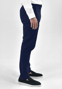 Navyblauwe broek met een slim fit, gemaakt van soepel materiaal, met een platte voorkant en zijzakken, gecombineerd met zwarte instapschoenen.