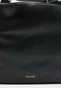 Schwarze, strukturierte Handtasche mit einem goldenen "LIU JO"-Logo auf der Vorderseite, das ein elegantes und stilvolles Design betont.
