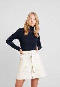 Marinblå polotröja med lång ärm i kombination med en krämfärgad, midjehögt denimsdottkjol som når knäna och har framknappar samt två sidofickor.