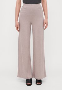 Pantalones de pierna ancha de tejido acanalado en rosa claro con una cinturilla alta, confeccionados en una tela suave, combinados con tacones abiertos negros.