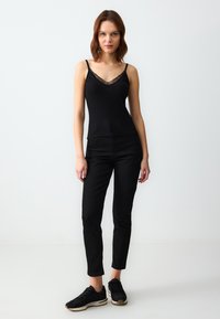 Zwarte camisole met kant, gecombineerd met zwarte aansluitende broek en zwarte sneakers. Minimalistisch design, soepele textuur en slanke silhouet.