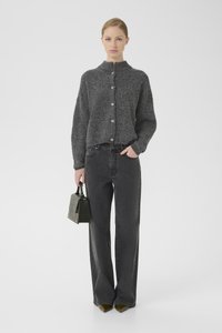 Grauer, strukturierter Cardigan mit hohem Kragen und Knopfverschluss, kombiniert mit hoch sitzenden schwarzen Jeans und einer kleinen schwarzen Handtasche.