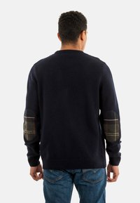 Marine gebreide trui met geribde onderrand en manchetten, voorzien van geruite elleboogpatches in groen en beige. Achteraanzicht, textiel met textuur.