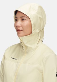 Wasserabweisende Mammt-Jacke in Hellgelb mit Kapuze, Frontreißverschluss und Logo auf der Brust. Strukturstoff mit Rautenmuster.