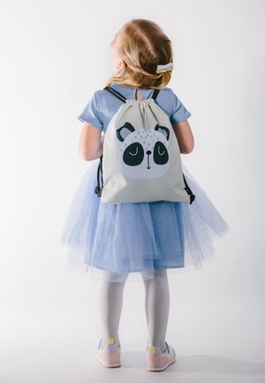 Gray drawstring backpack with panda face graphic. Child wearing blue dress with tulle skirt, silver leggings, and multi-colored shoes.