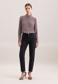 Chemise à manches longues boutonnée de couleur bordeaux avec un petit motif blanc, associée à un jean en denim noir taille haute et des sandales à talons noires.