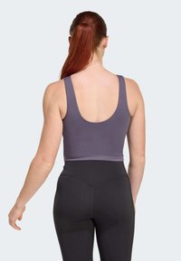 Grauer sportlicher Crop-Top mit breiten Trägern und rundem Rückenausschnitt, kombiniert mit hochgeschnittenen schwarzen Leggings, die aus glattem Material mit minimalen Nähten bestehen.