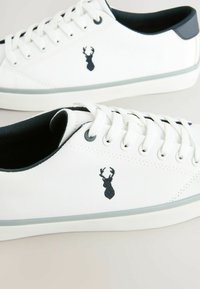 Witte canvas sneakers met zwarte accenten en een blauw hert logo. Bevat een vetersluiting, gestructureerde stof en een rubberen zool.