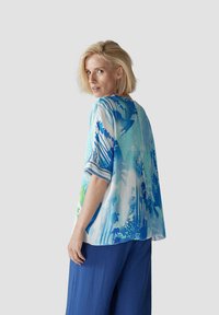 Leichtes, kurzärmliges Oberteil mit einem blau-grünen abstrakten Muster, aus einem transparenten Stoff mit einem lockeren, fließenden Design.