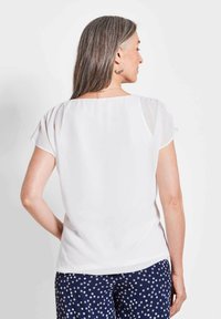 Weiße Bluse mit kurzen Ärmeln, glatter Textur und quadratischem Rückenausschnitt, kombiniert mit marineblauen Hosen mit weißen Polka-Dots.