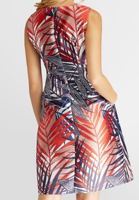 Robe sans manches avec un imprimé botanique rouge, marine et blanc, fabriquée en tissu doux, dotée de poches latérales et d'une fermeture éclair dissimulée au dos.