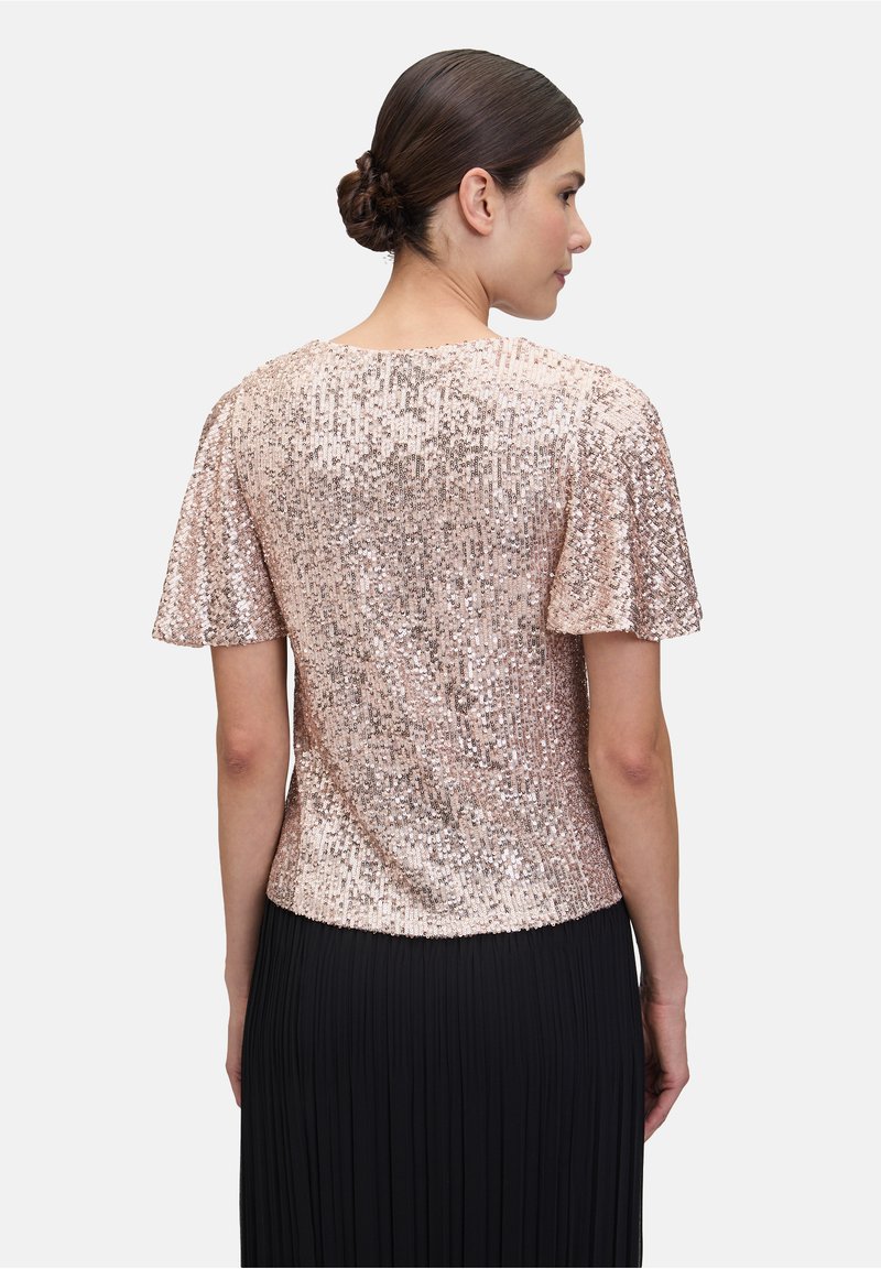 Top in paillettes rosa antico con maniche a farfalla corte, caratterizzato da una silhouette aderente e una texture liscia, abbinato a una gonna nera plissettata.