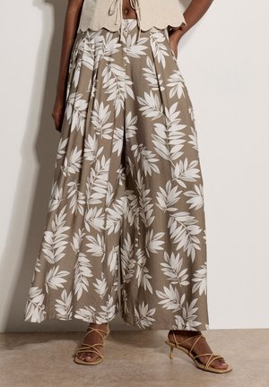 Beige, weit geschnittene Hose mit weißem tropischem Blattmuster, kombiniert mit nudefarbenen Riemchensandalen mit Absatz und einem bauchfreien Top, das an der Taille gebunden ist.