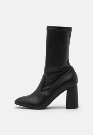 Bottine noire en cuir texturé, avec un bout pointu et un large talon haut. Le design comprend une tige ajustée avec une couture subtile.