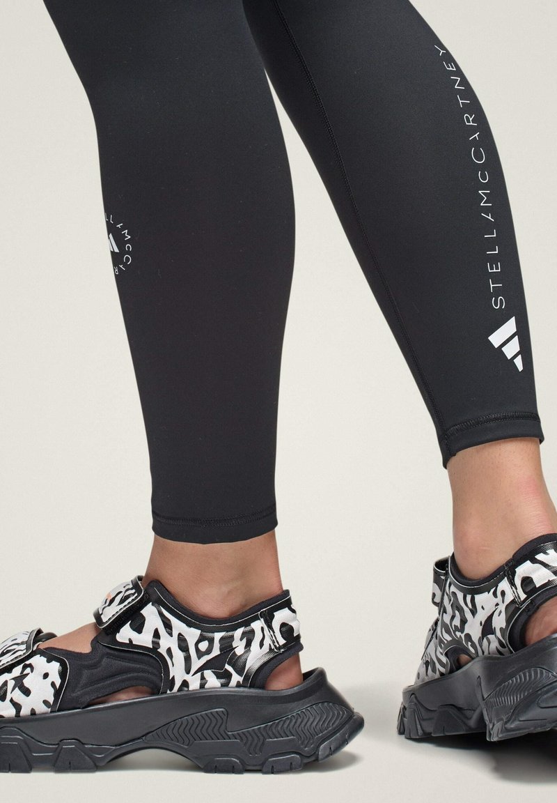 Zwarte leggings met witte logodetails, gecombineerd met zwart-witte dierenprint sandalen met verstelbare banden en gegoten zolen.