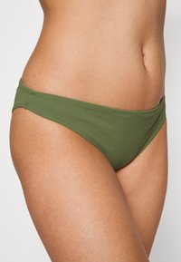 Parte de baixo de biquíni verde oliva feita de tecido macio. Apresenta cobertura mínima com uma cintura sem costura e textura suave.