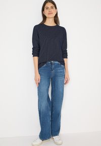 Granatowa bluzka z długim rękawem o fakturowanej powierzchni w połączeniu z jasnoniebieskimi, szerokimi jeansami i białymi sneakersami. Strój cechuje się swobodnym, luźnym krojem.