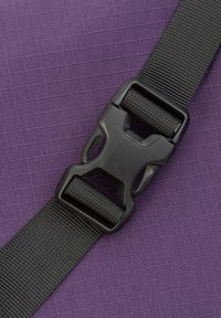 Nahaufnahme einer schwarzen Schnalle und einem Riemen vor einem strukturierten lila Hintergrund, der den Verschlussmechanismus hervorhebt.