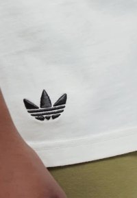 Bílý bavlněný tričko s černě vyšitým logem Adidas, které je doplněno třemi lístkovými akcenty a vodorovnými pruhy na spodní části.