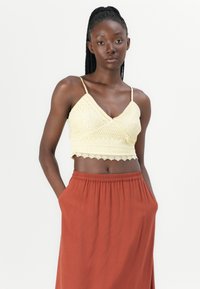 Háčkovaný crop top ve světle žluté barvě s krajkovým lemem. V kombinaci s rustově zbarvenou sukní s elastickým pasem. Oblečení má tenké ramínka.