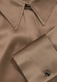 Col et manchette de chemise en satin marron avec bouton noir, montrant une texture de tissu lisse et des détails de couture soignés.