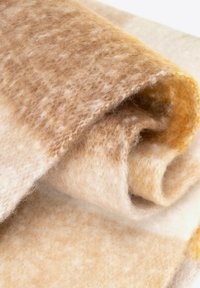 Brązowy i kremowy wełniany koc o miękkiej fakturze, częściowo zwinięty, ukazujący gradientowy wzór łączący jaśniejsze i ciemniejsze odcienie.