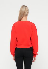Sweatshirt rouge avec un design court, des poignets larges et un col rond. Associé à un jean skinny noir, montrant une texture lisse.