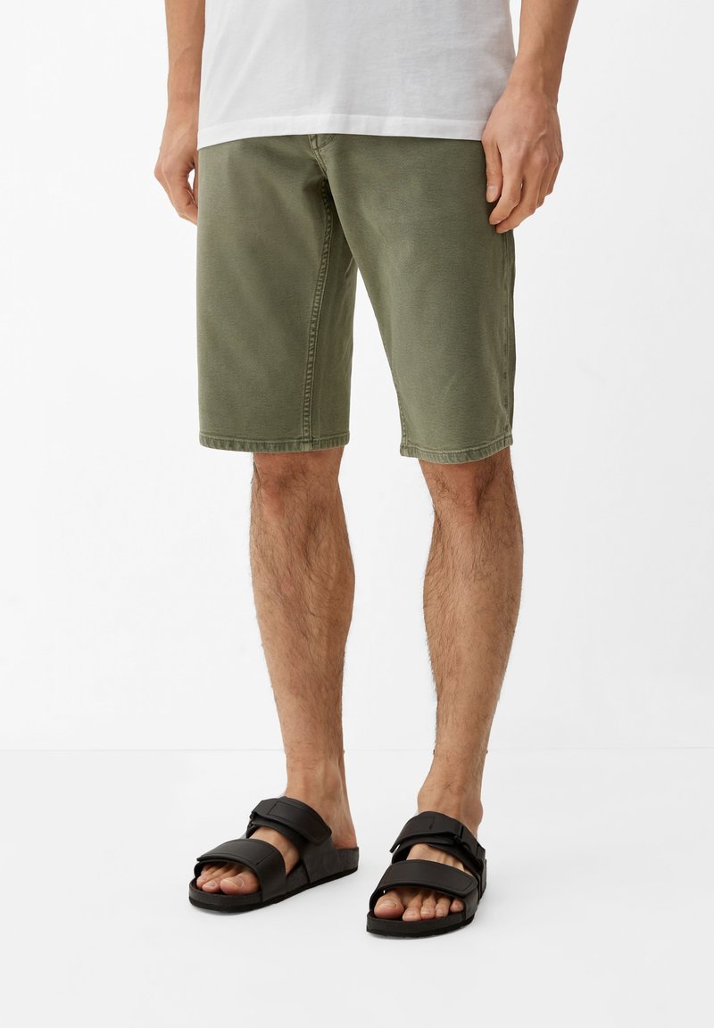 Oliwkowe bawełniane szorty o prostym kroju z wykończonym dołem, zestawione z czarnymi sandałami z regulowanymi paskami.