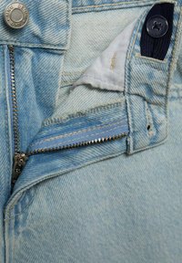 Material de denim bleu deschis cu fermoar și închidere cu buton; prezintă o mică buzunar interior cu un buton închis la culoare și cusături vizibile.