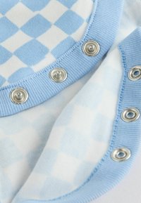 Blau kariertes Gewebe mit hellblauen und weißen Quadraten, versehen mit silbernen Druckknöpfen am Ausschnitt. Weiche, gestrickte Textur.