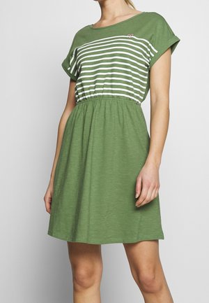 Mujer con un vestido verde, con rayas horizontales blancas en la parte superior y mangas cortas remangadas, cintura elástica y falda hasta la rodilla.