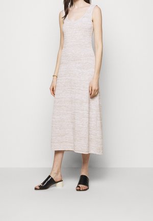 Strick, ärmelloses Midikleid in hellem Beige mit einem strukturierten Muster. Kombiniert mit schwarzen Sandalen mit einem weißen Absatz.