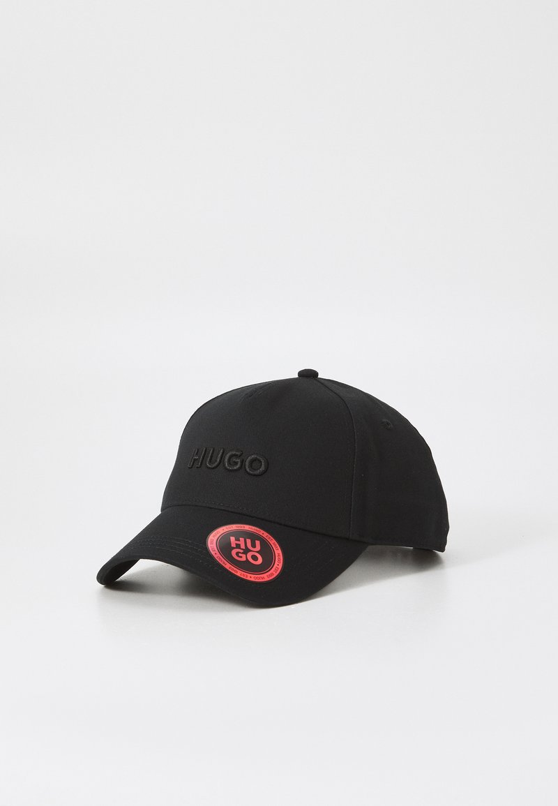 Svart baseballcap med brodert "HUGO"-logo, buet skjerm og en rund rød etikett med "HUGO." Laget av slitesterkt stoff.