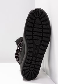 Semelle extérieure en caoutchouc noir avec un motif de traction texturé. Lacets tissés noirs et blancs et une partie supérieure douce. Matériel de fixation visible.