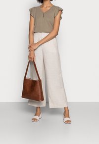 Brązowa skórzana torba tote, jasnobrązowy top w serek z krótkimi falbaniastymi rękawami, beżowe szerokie spodnie oraz kremowe sandały na ramiączkach.