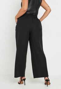 Pantalones de pierna ancha negros con cintura elástica, que presentan una textura suave y bolsillos laterales, combinados con sandalias de tacón alto negras.