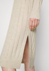Stickad klänning i beige med vertikal ribbad textur, med en sidöppning och åtsittande ärmslut. Mjuk, flexibel material med en ren finish.