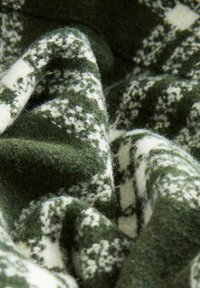 Knit fabric in dark green with white geometric patterns. Soft texture with a fuzzy finish, creating depth and visual interest.