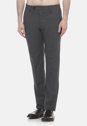 Uomo con pantaloni eleganti grigio scuro e mocassini in pelle nera, in piedi su uno sfondo bianco uniforme.