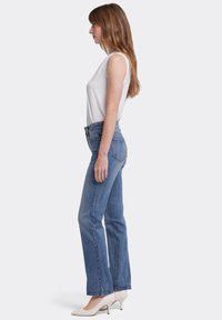 Lichtblauwe denim jeans met een rechte pijp, gecombineerd met een witte mouwloze top en crèmekleurige hoge hakken. Zichtbare sproeten op de arm.