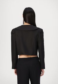 Blazer nero sagomato con un colletto pronunciato, spalle strutturate e tessuto liscio, abbinato a pantaloni neri a vita alta.